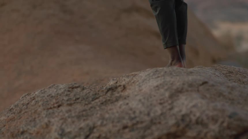 A woman walks barefoot up a large rock in a canyon