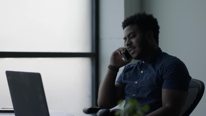 A man sitting by a laptop answers his phone