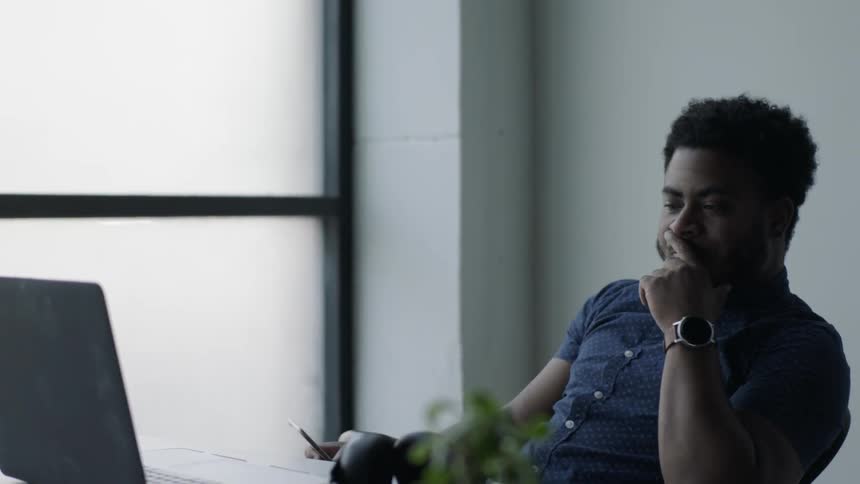 A man in a blue shirt ends his call and leans back