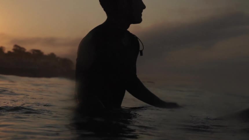 A man rides a surfboard at sunset