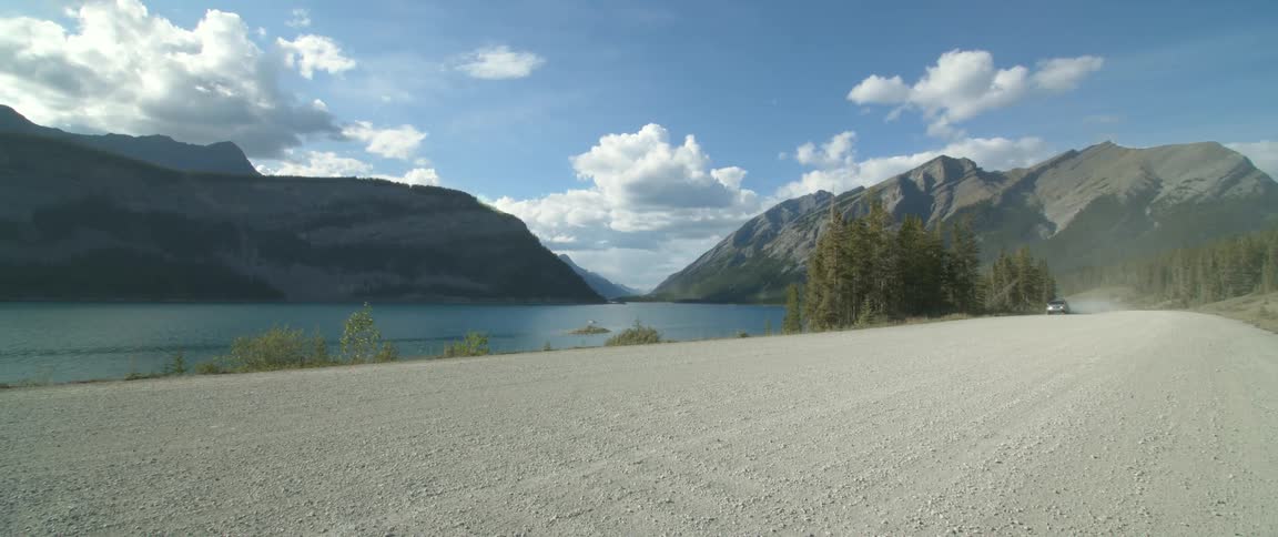 A car drives along the shore on a dirt road