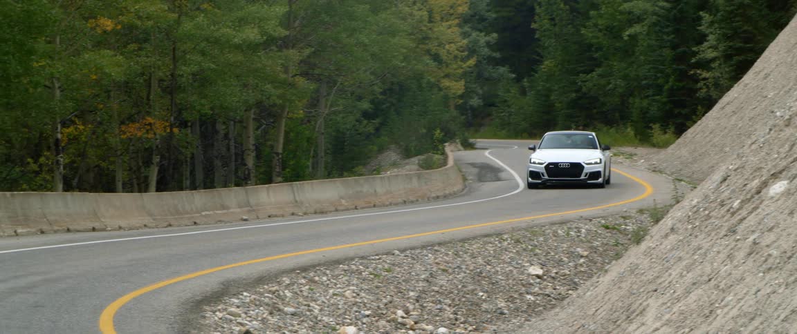 A man drives down a winding road past a forest