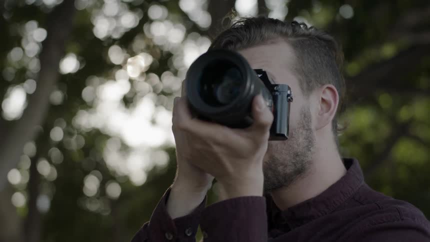 A man lifts a camera and adjusts the lens