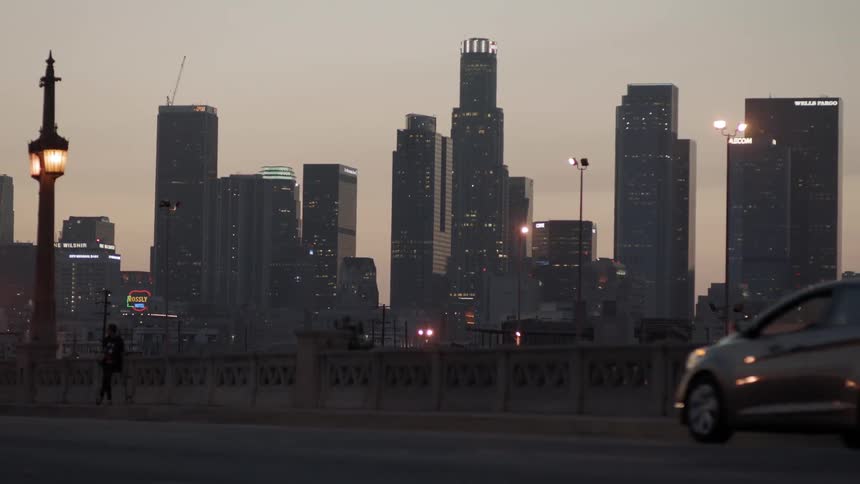 Cars drive on a bridge near a city at sunset