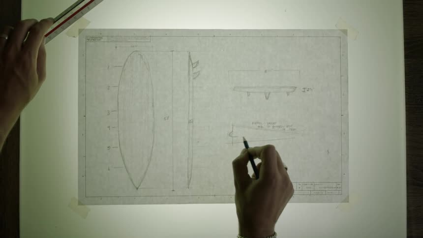 A person sketches on a piece of paper taped to a light board
