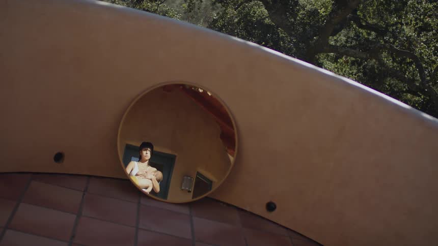 A round mirror reflecting a woman holding a baby outside