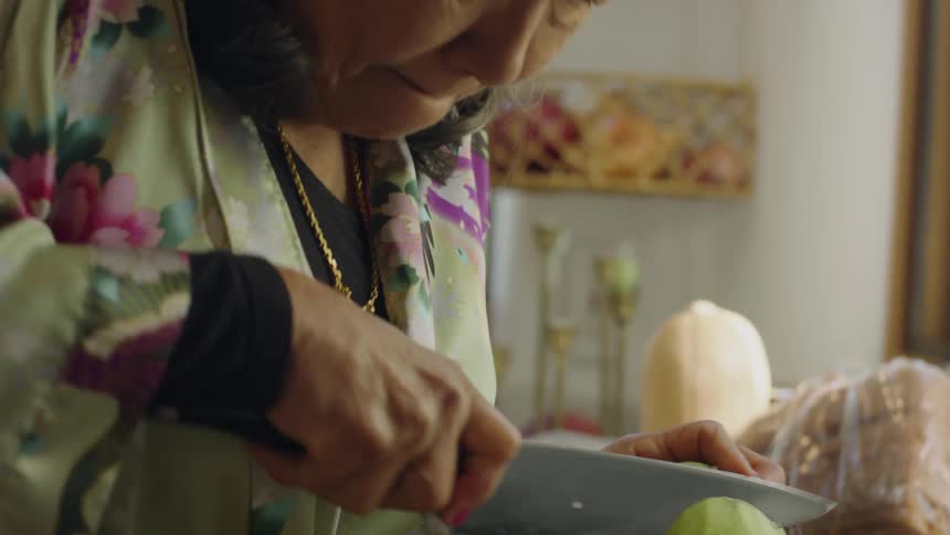 Grandmother uses a sharp kitchen knife to slice a cabbage on the kitchen at home
