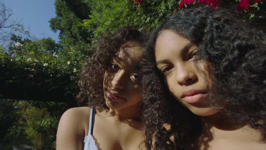 Two young girls with curly hair standing in the garden outdoors looking at the camera in