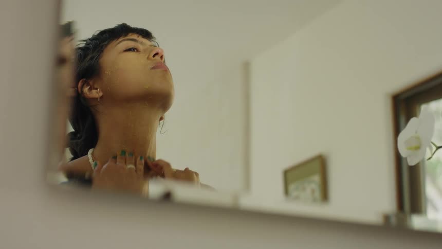 Face rubs lotion onto her face while looking into mirror