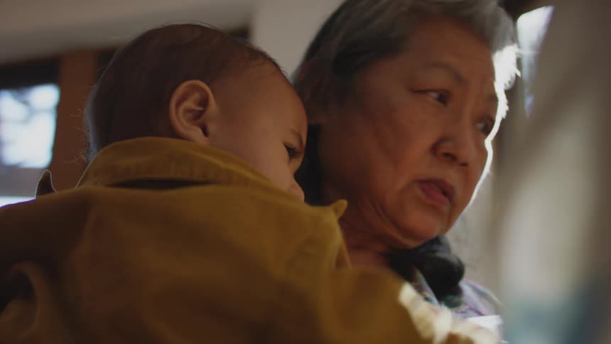Grandmother helps mother to feed a child in the kitchen at home