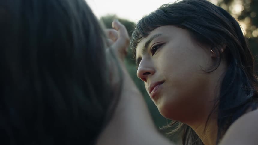 A teenage girl sits outside and strokes another girls hair and face