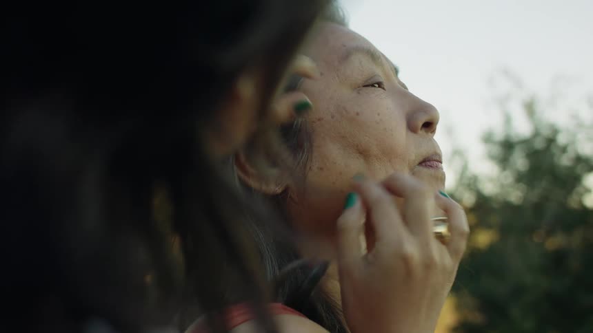 Daughter massages her mother face with her fingers while sitting outdoor at morning