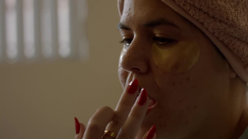 Woman wearing towel on head holds mouth open as another smooths out lips