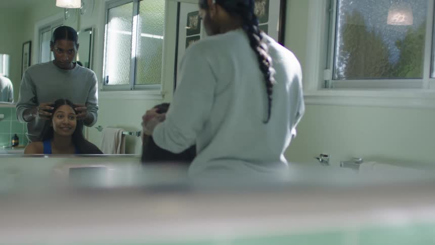 A man stands behind a woman in a bathroom and runs his fingers through her hair