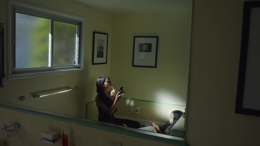Girl with straight black hair puts on makeup and girl takes selfie with red smartphone in bathtub in the bathroom