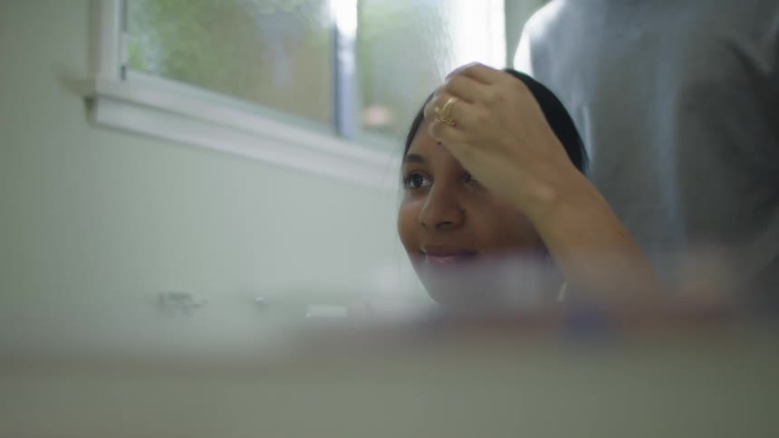 Young woman sitting in front of a mirror gets a maang tikka placed on her forehead