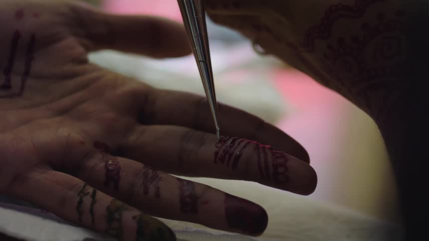 Person decorates another persons hand with patterns made with henna
