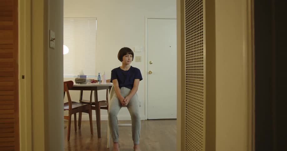A girl sits at the table thinking then looks up and smiles as her mother enters and caresses her hair