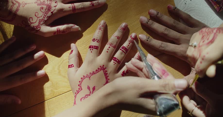 Group of people applying henna ink tattoos on the hands of friends or customers over a table