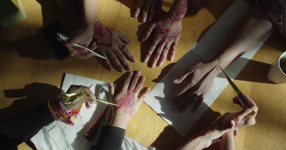 Group of people applying henna ink tattoos on the hands of friends or customers over a table