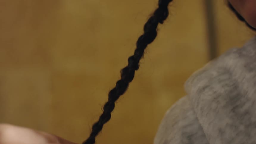 Woman braids girls hair wearing gray hoodie