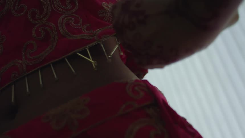 A woman putting on ornate clothing with patterns and beads