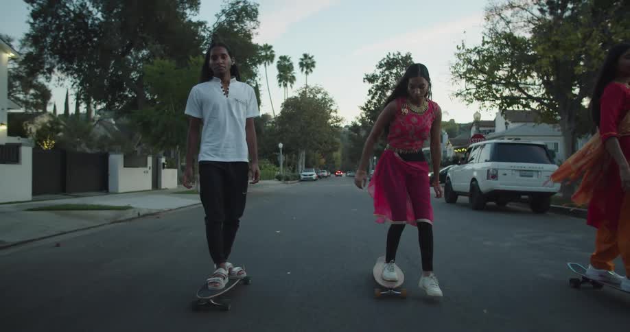 Girls wearing traditional indian garments riding skateboards on the neighborhood at sunset