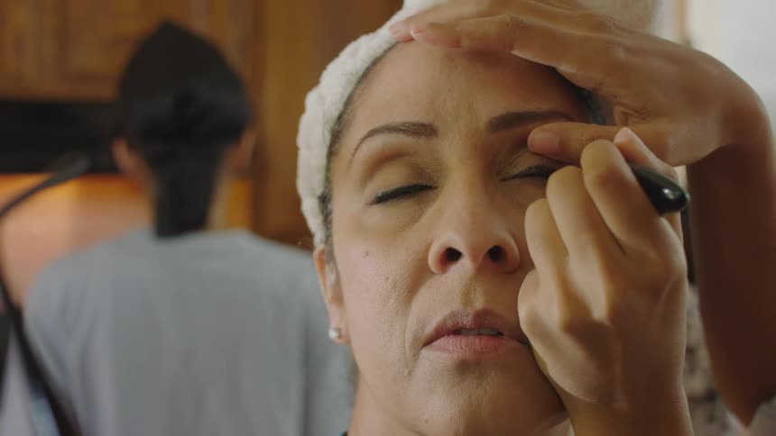 People are in a kitchen and applying makeup to their face