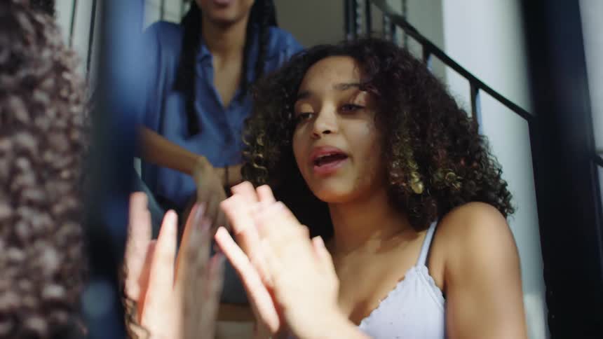 Teenagers play a hand game on a stoop while a couple women watch