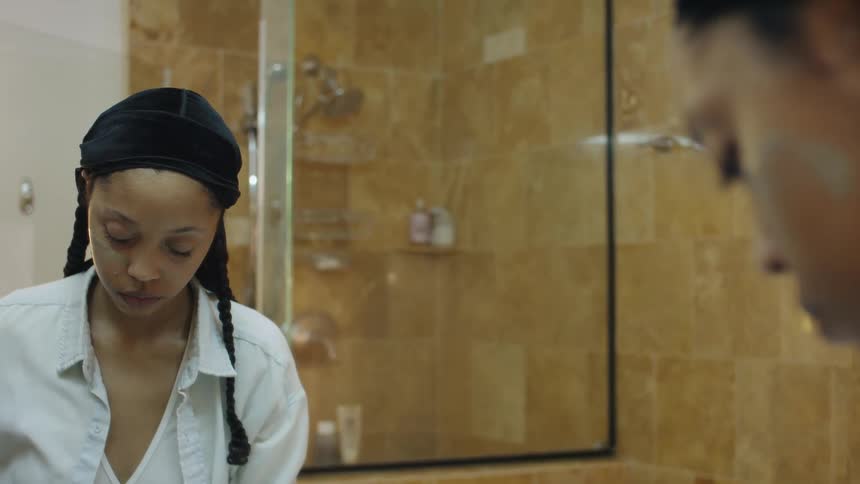 A teenager applies cream to her face in a bathroom