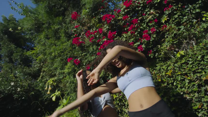 Two women in sports bras posing outside near flower bushes