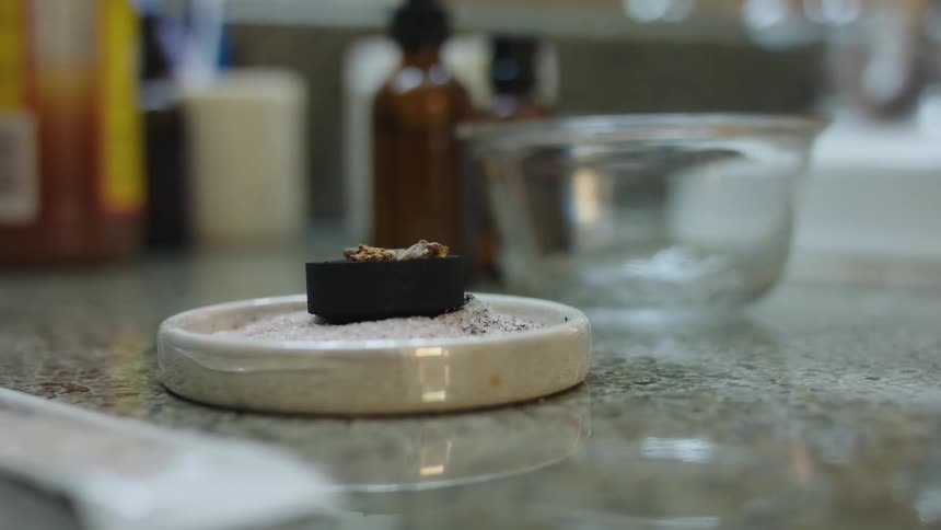 Hand places incense over a burning charcoal puck over the sand inside a ceramic plate