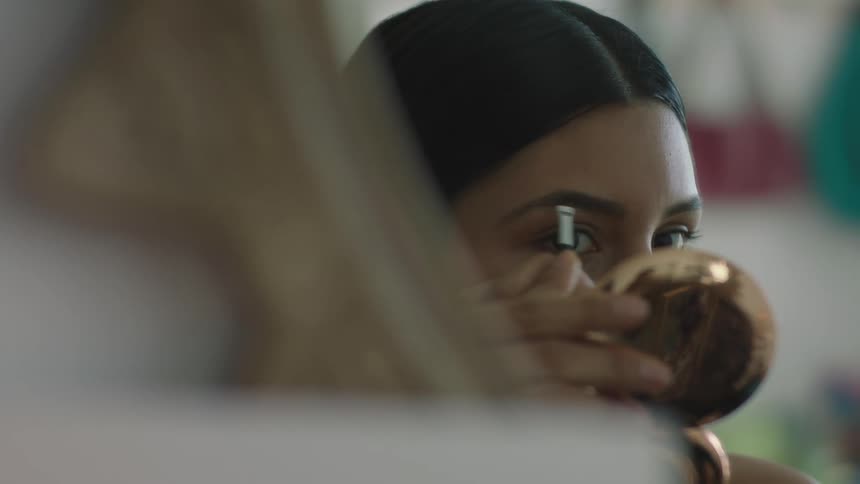 A woman is looking in the mirror and applying makeup