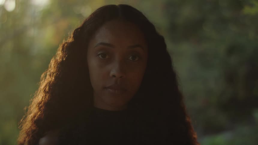 A teenage girl in a forest turns her head and looks ahead of her