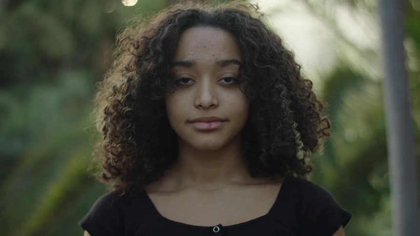 Girl with curly hair and black blouse looks at camera smiling