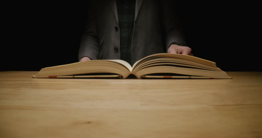 Man with gray blazer and green shirt turns over book pages in dark room