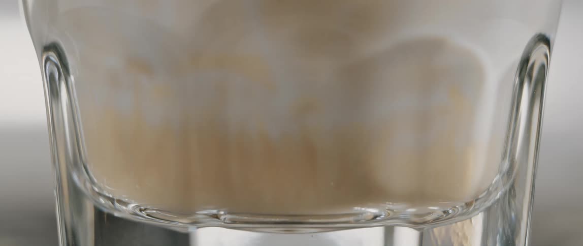 Brewed coffee is poured into a glass of steamed milk to create a latte at a cafe