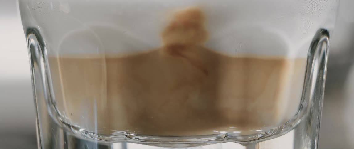 Brewed espresso coffee is poured into a glass of steamed milk to create a latte at a cafe