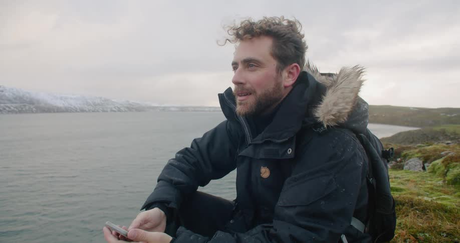 A man is sitting by the coast with his cellphone