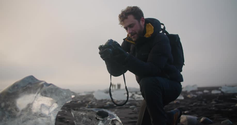 Young man takes pictures of the ice on diamond beach in Iceland