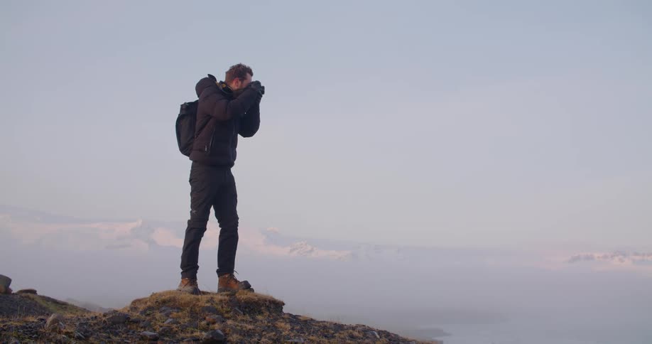 A man is standing on rocky terrain and taking pictures of nature