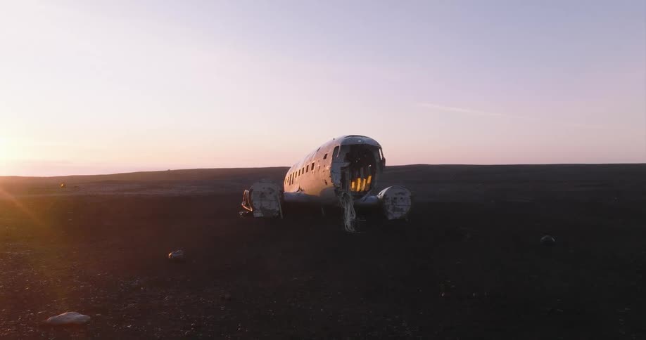 Sunlight shines from horizon onto wrecked plane sitting on dirt field