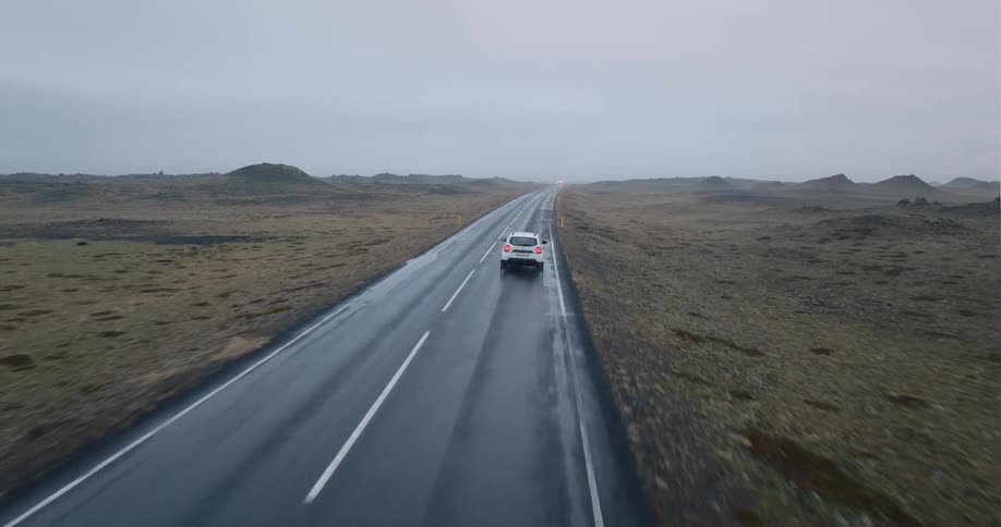 Automobiles travel on a wet rural road with the headlights on