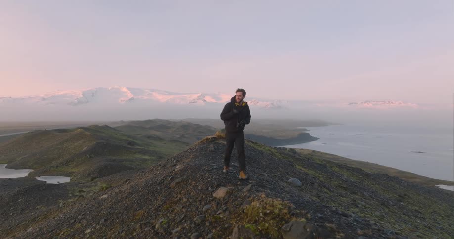 A man in a winter coat walks along the top of a hill overlooking the ocean during the day