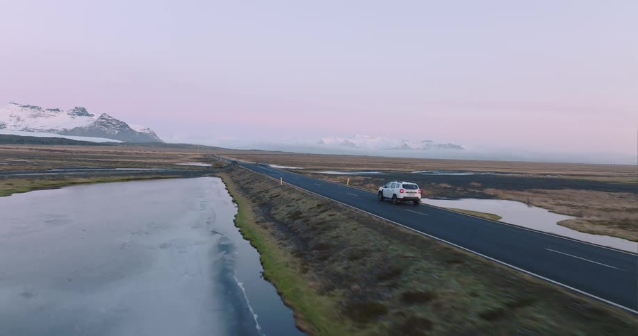 A white suv travels on an empty road towards mountains