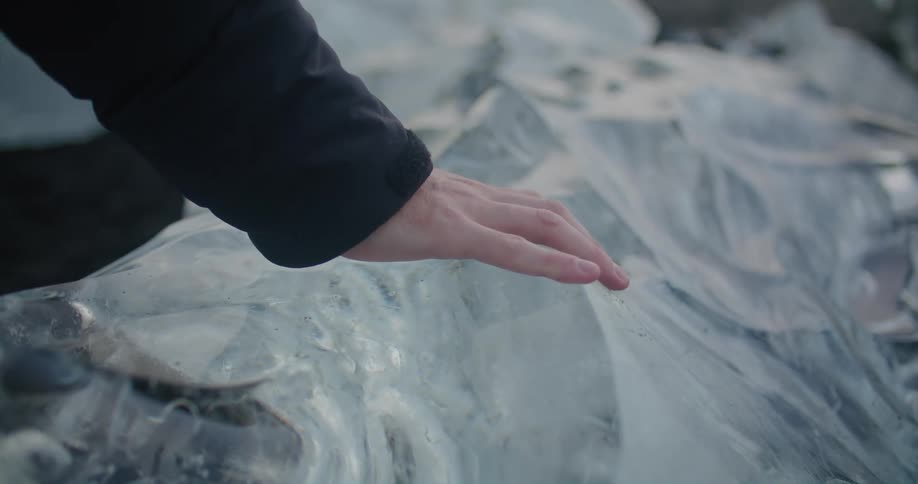 A person runs their hand along a large chunk of ice