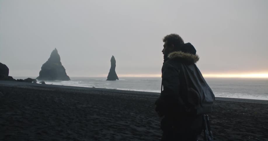 A man is walking along the beach at dusk