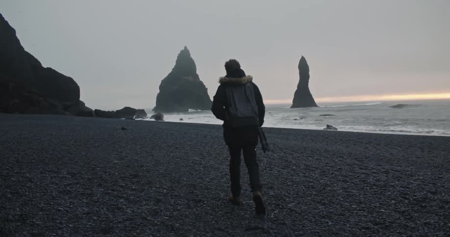 A man walks on a rocky beach toward ocean waves and rock formations