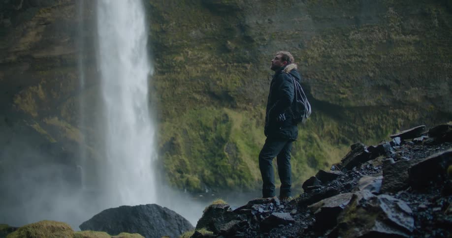 A male hiker next to a waterfall in nature on a cold day