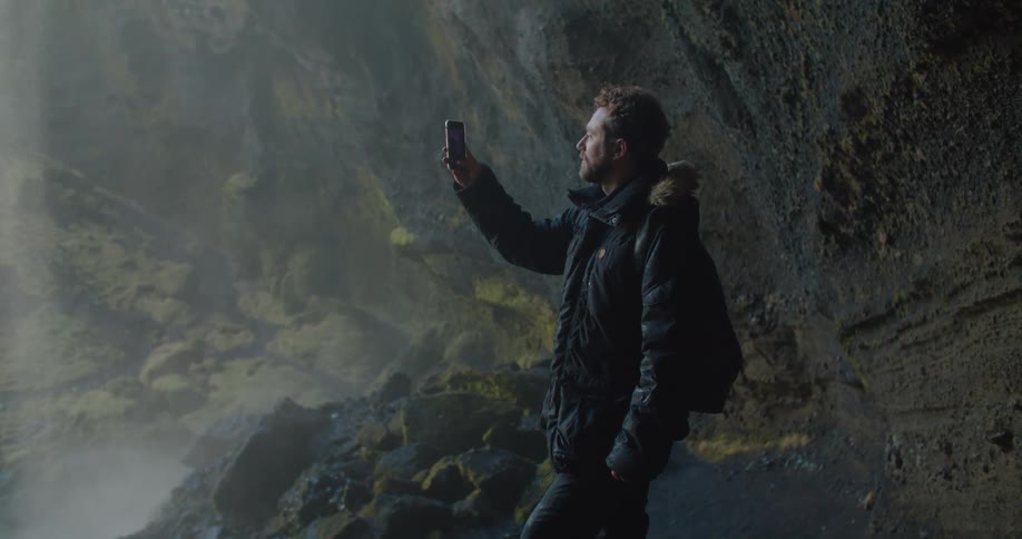 A man is taking pictures of a waterfall with his cellphone